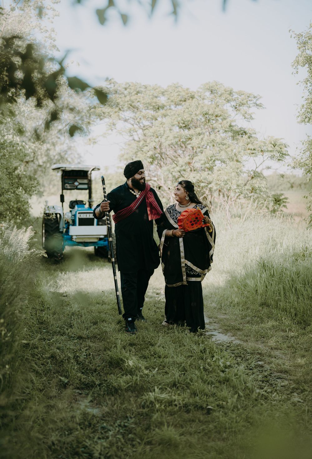 Couple in traditional Indian dress walking together in a rustic outdoor setting with vehicle in background.