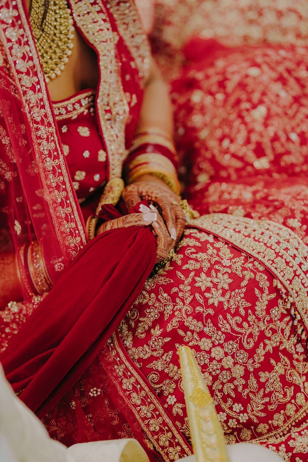 Close-up detail of red and gold embroidered lehenga with traditional Indian bridal jewelry and henna.