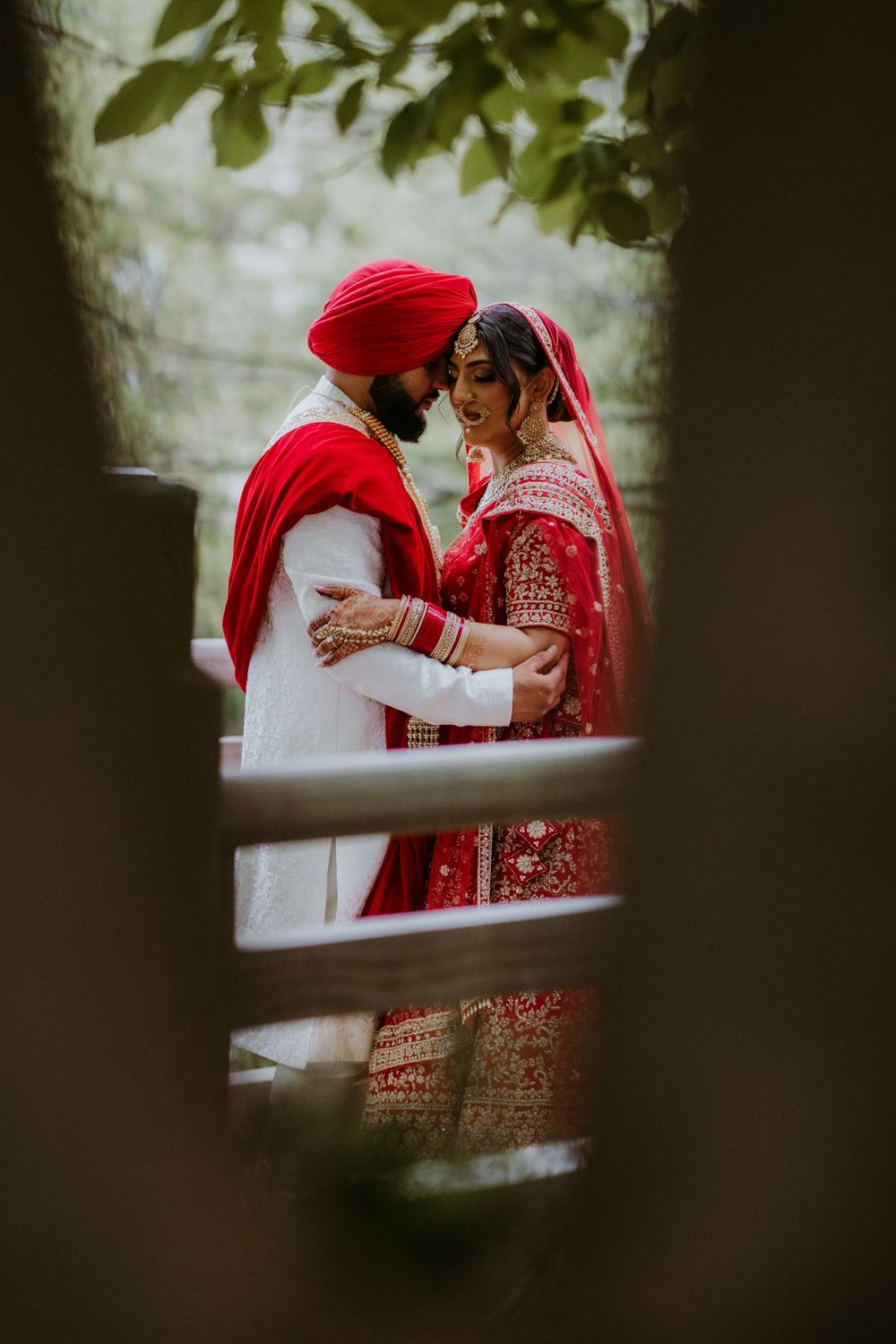 An intimate moment captured through foliage of a couple in traditional Sikh wedding attire.