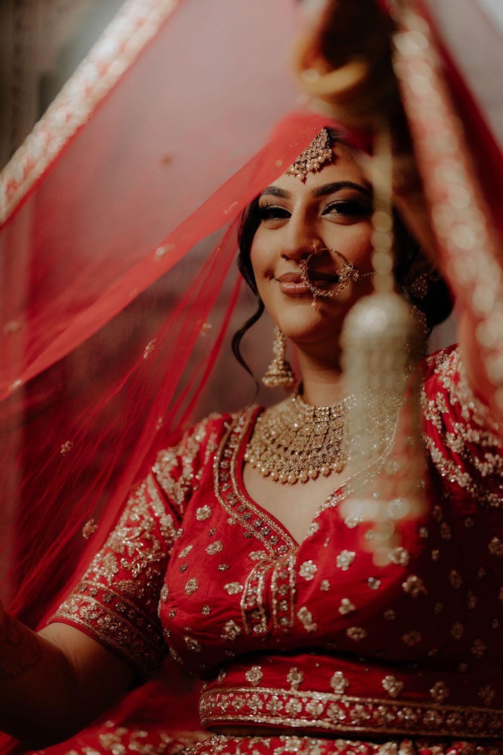 A traditional Indian bridal portrait with red attire and intricate gold jewelry.
