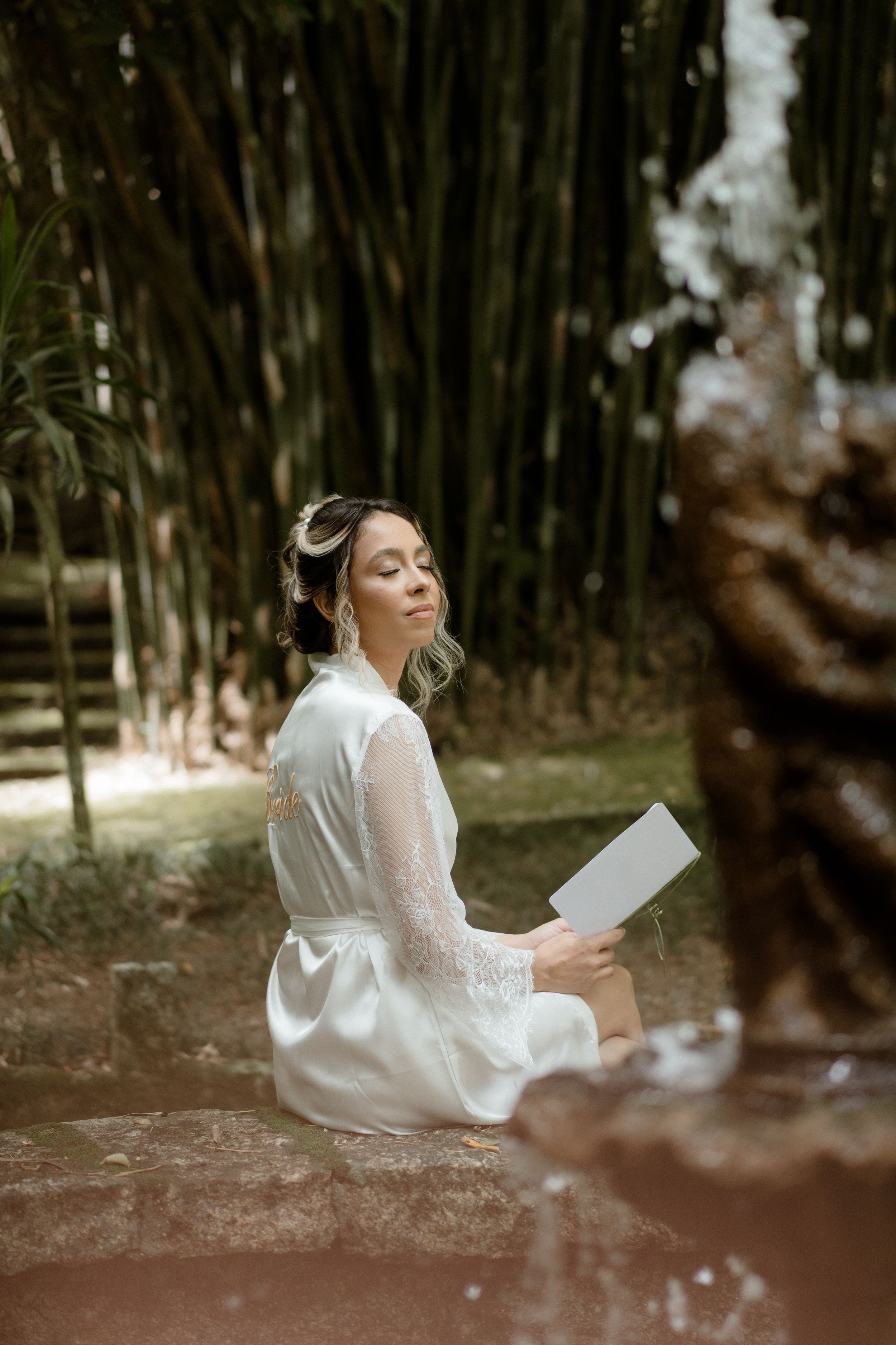 A person in a white lace robe sits peacefully reading in a bamboo garden setting.