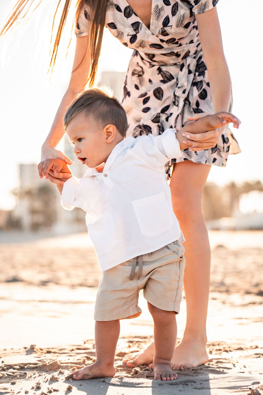 mom helping young boy to walk on the sand at the beach during family photos