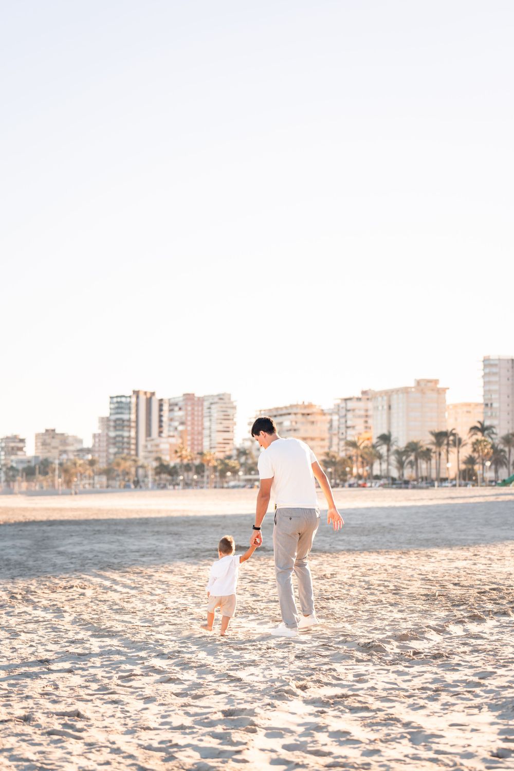 young boy and dad running along the beach in the golden fine sand in playa de san juan alicante