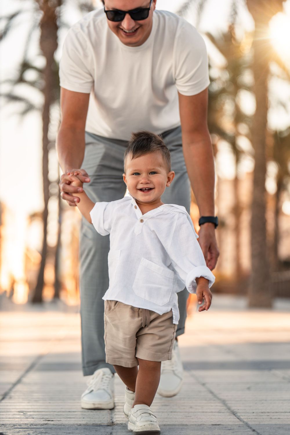 boy smiling and running with dad on promenade along playa san juan alicante beach