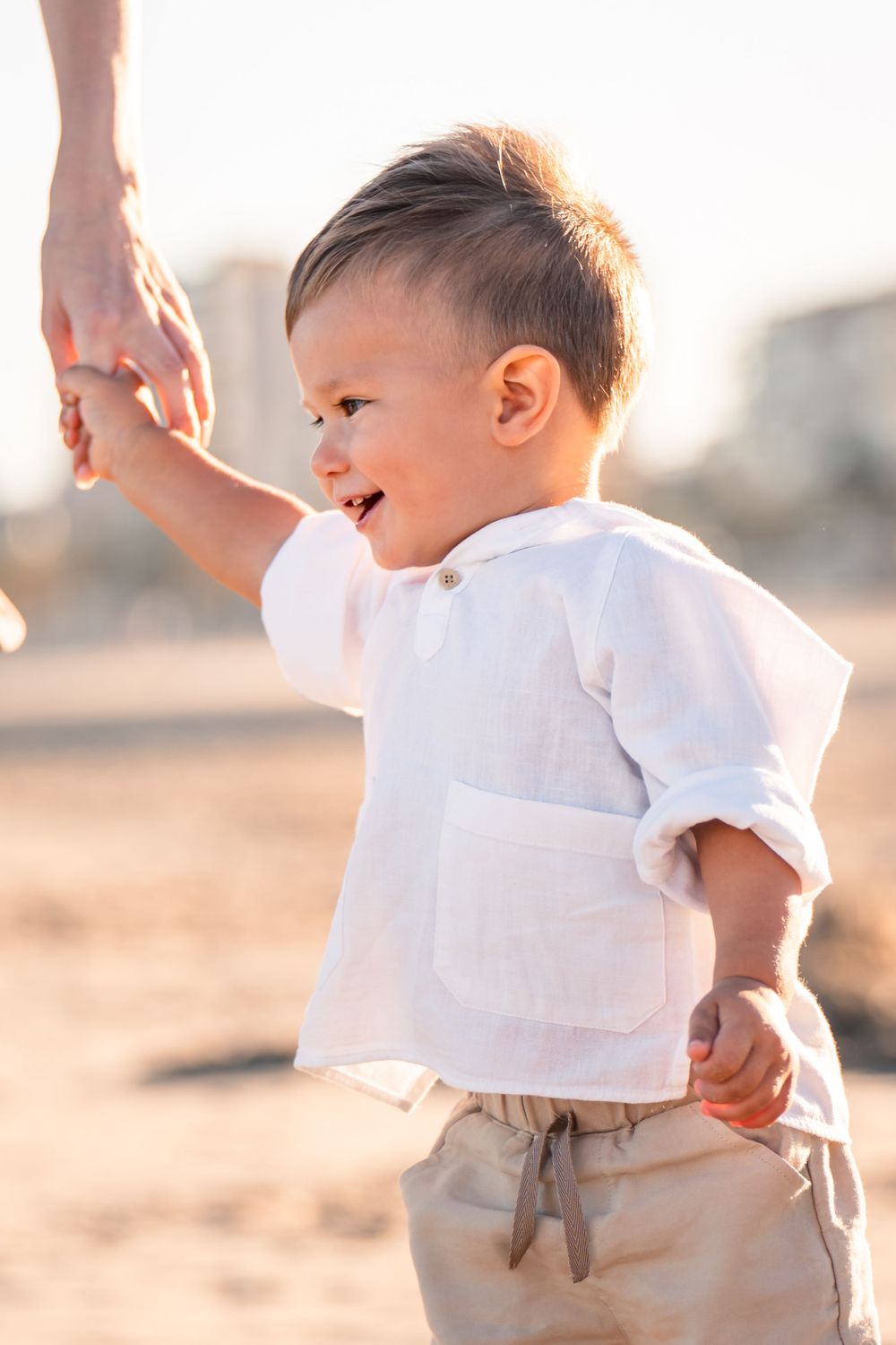young boy smiling and holding dads hand while walking on the beach in alicante playa san juan