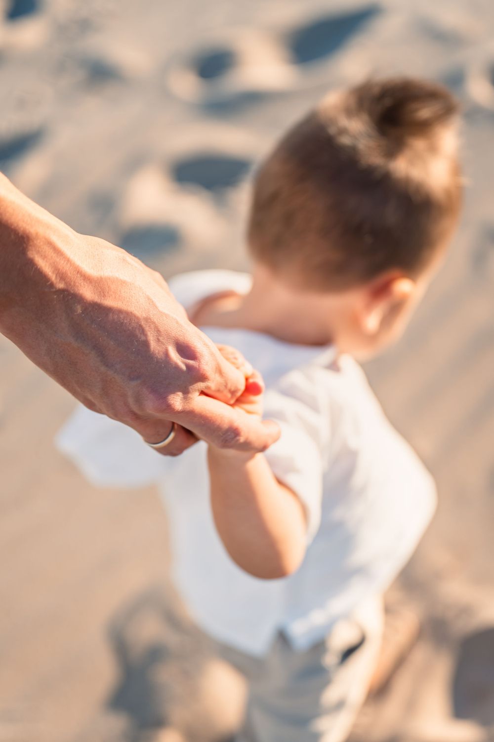 dad holding young boys hand to help him walk on the beach