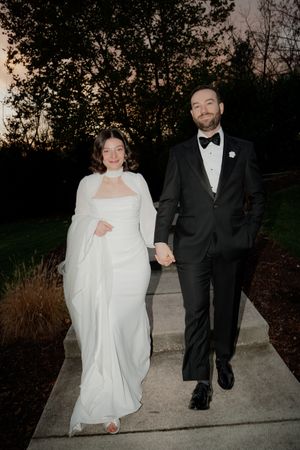 A couple walking together on a concrete path at dusk, with the person in white trailing behind playfully.