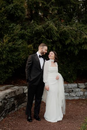 A romantic moment between a couple outdoors with stone walls and greenery in the background.