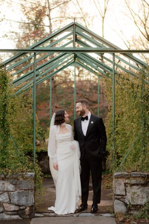 A couple shares a romantic moment in a vintage greenhouse with climbing vines and glass walls during their wedding day.