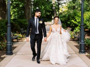 Wedding couple walking along a path with ornate lampposts, bride in a stunning lace gown.