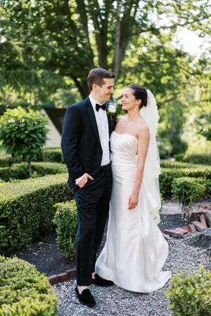 Couple in formal wedding attire standing in manicured garden path.