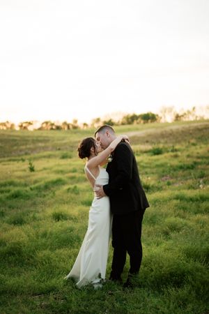 A couple shares an intimate moment on a grassy hillside during sunset.
