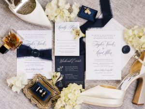 Wedding invitation suite with navy accents, white hydrangeas, and elegant bridal shoes on linen background.