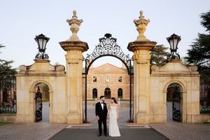 Bride and groom posing before ornate iron gates at a grand historic estate venue at dusk.