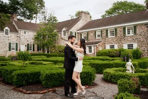 A romantic dance pose in a formal garden path with stone mansion and manicured hedges as backdrop.