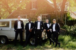 Wedding party poses casually outdoors by vintage vehicles in elegant black and white attire.