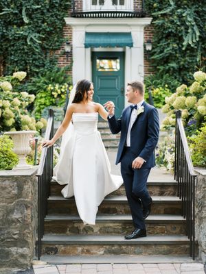 Couple poses on stone steps with hydrangea bushes and teal door in background.
