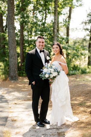 Sunny outdoor wedding portrait with blue and white floral bouquet.