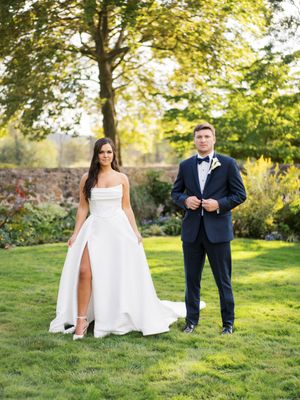 An elegant wedding portrait of a couple standing on manicured lawn with trees in the background.