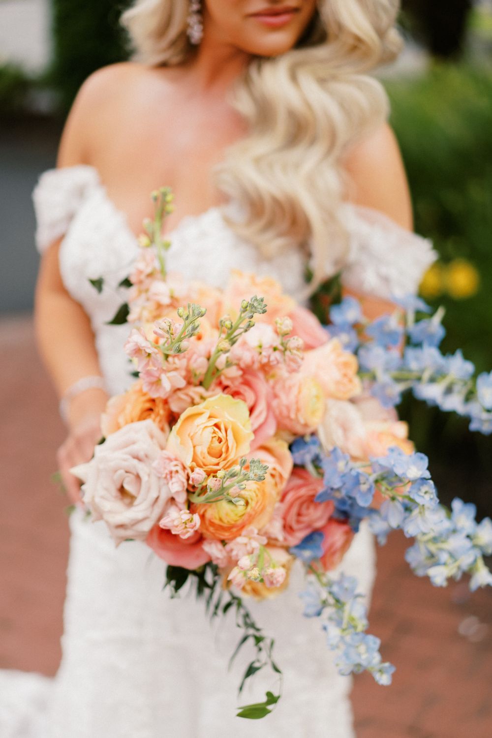 Close-up of vibrant coral and blue wedding bouquet against white lace bridal gown.