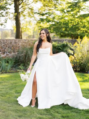 A joyful bride in a flowing white gown twirls on a sunlit garden lawn.