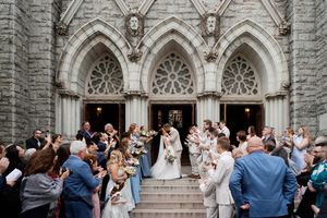 Wedding celebration outside historic stone church with gothic arched doorways as guests line the stone steps.