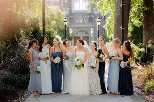 Wedding party in light blue and navy dresses pose together in a scenic outdoor garden setting.