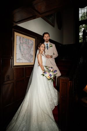 A newlywed couple stands in a dimly lit church interior with an antique map of North America displayed on the wall behind them.