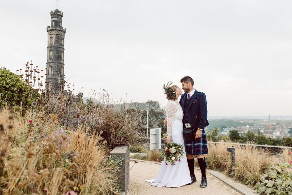 Stone tower and path with blooming flowers overlooking Edinburgh cityscape.
