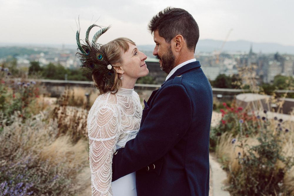 Romantic wedding couple embracing on scenic overlook with city views.