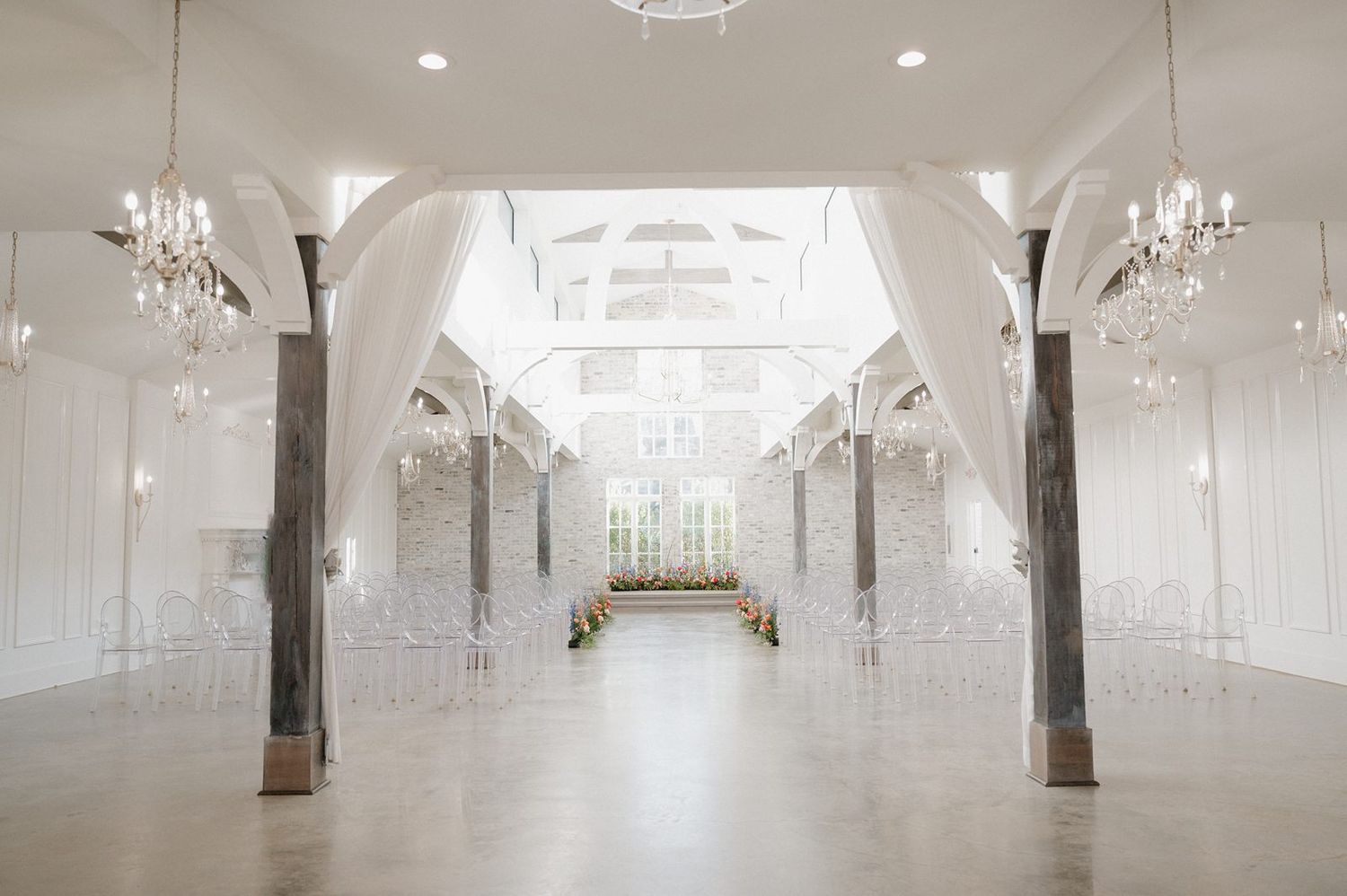 Elegant white wedding venue with crystal chandeliers, exposed wooden beams and natural light streaming through skylights.