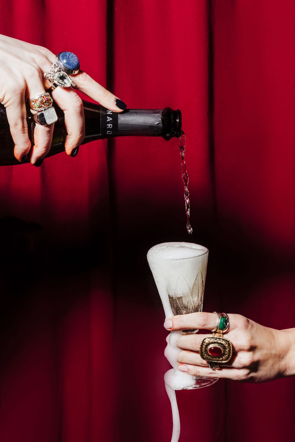 Champagne being poured into foaming glass against dramatic red curtain backdrop.