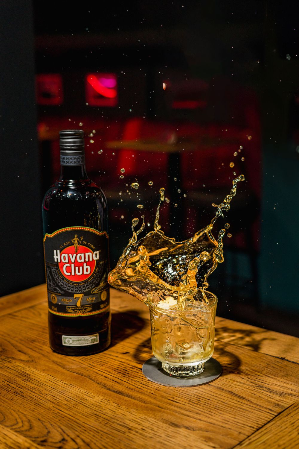 Havana Club rum bottle with splashing liquid in glass on wooden surface.