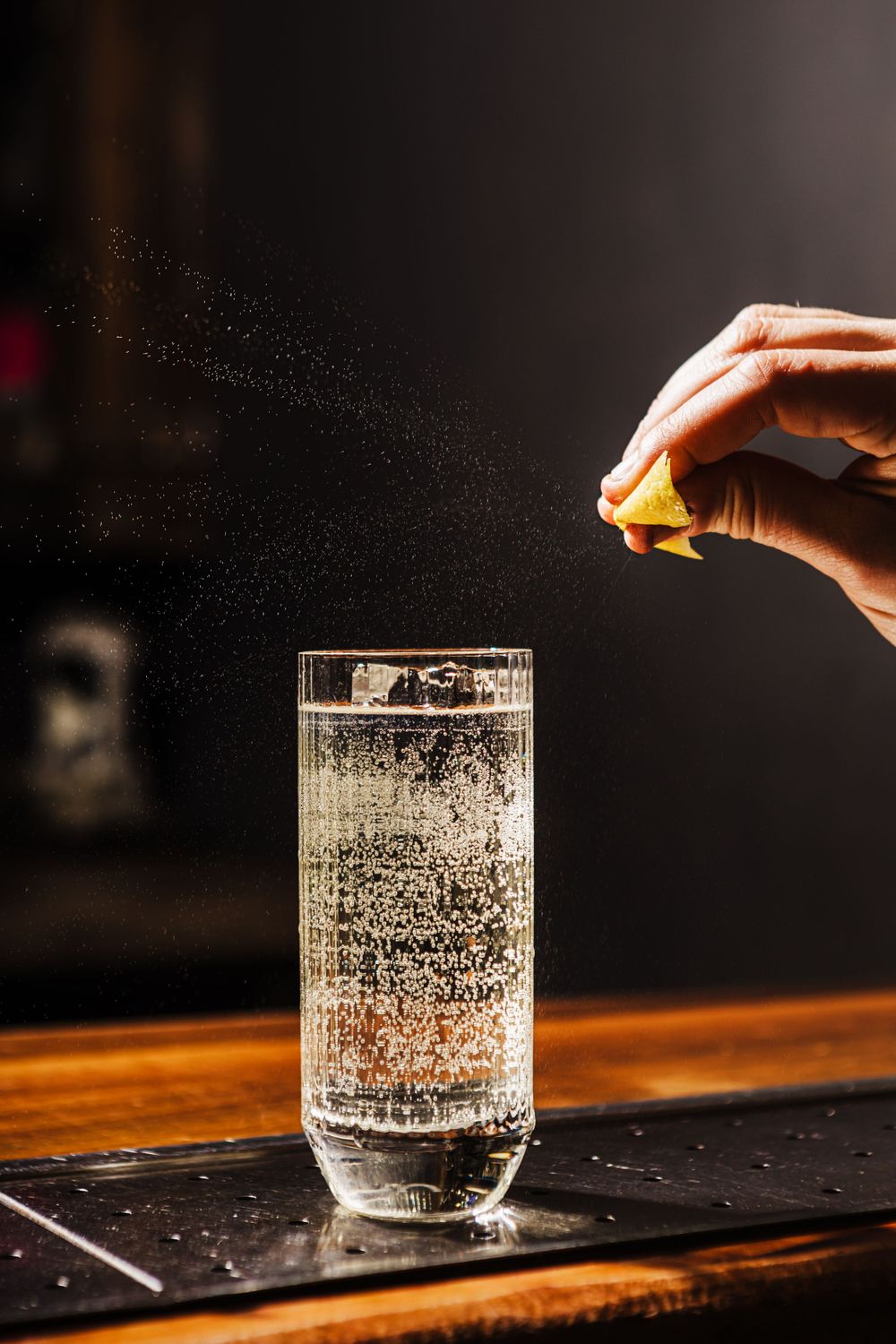 Citrus being squeezed over a tall glass of sparkling beverage on wooden surface.