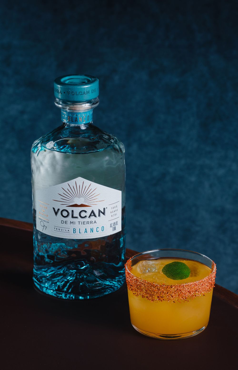 Volcan tequila bottle next to yellow cocktail with rimmed glass.