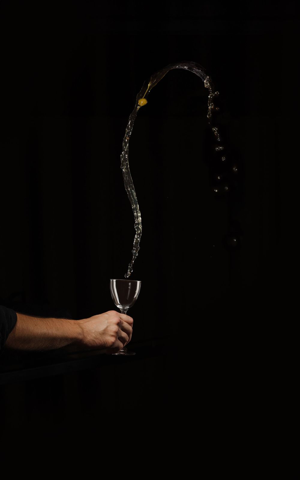 Dramatic splash of liquid arcing through darkness into a wine glass.