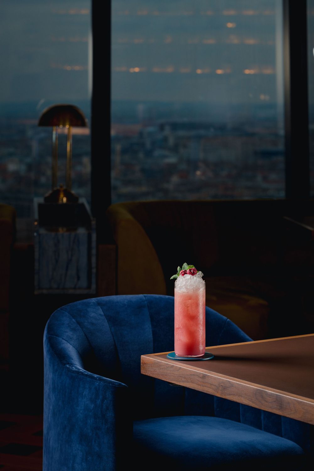Pink cocktail with whipped cream in tall glass on wooden table with city view.
