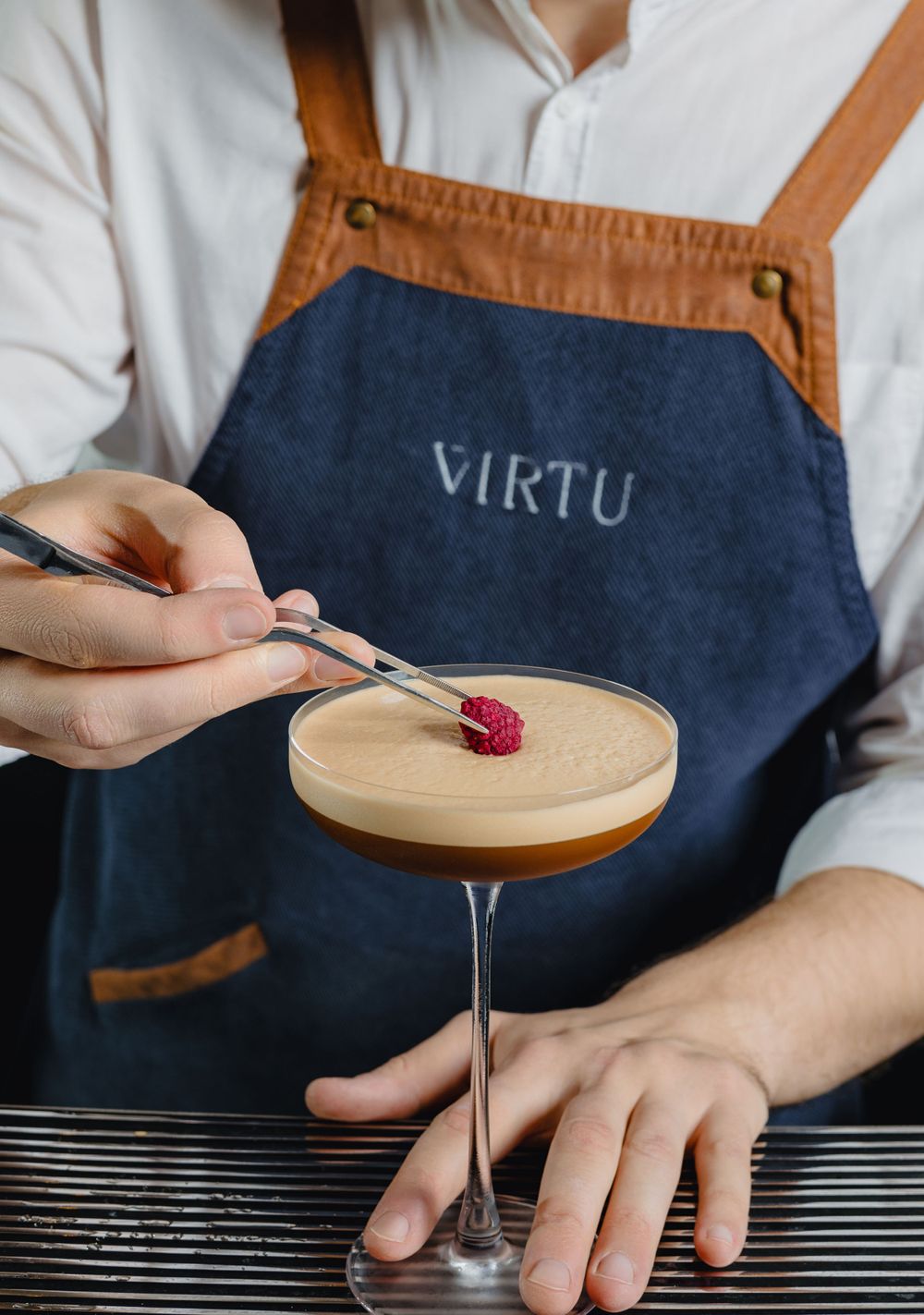 Cocktail garnished with raspberry in coupe glass on dark surface.