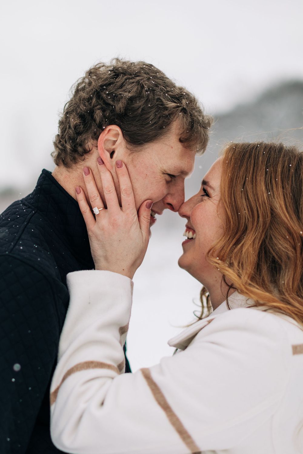 An intimate romantic moment captured between a couple in the snow with joyful expressions.