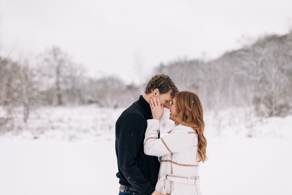 A tender winter engagement scene with a couple embracing in a snowy field.