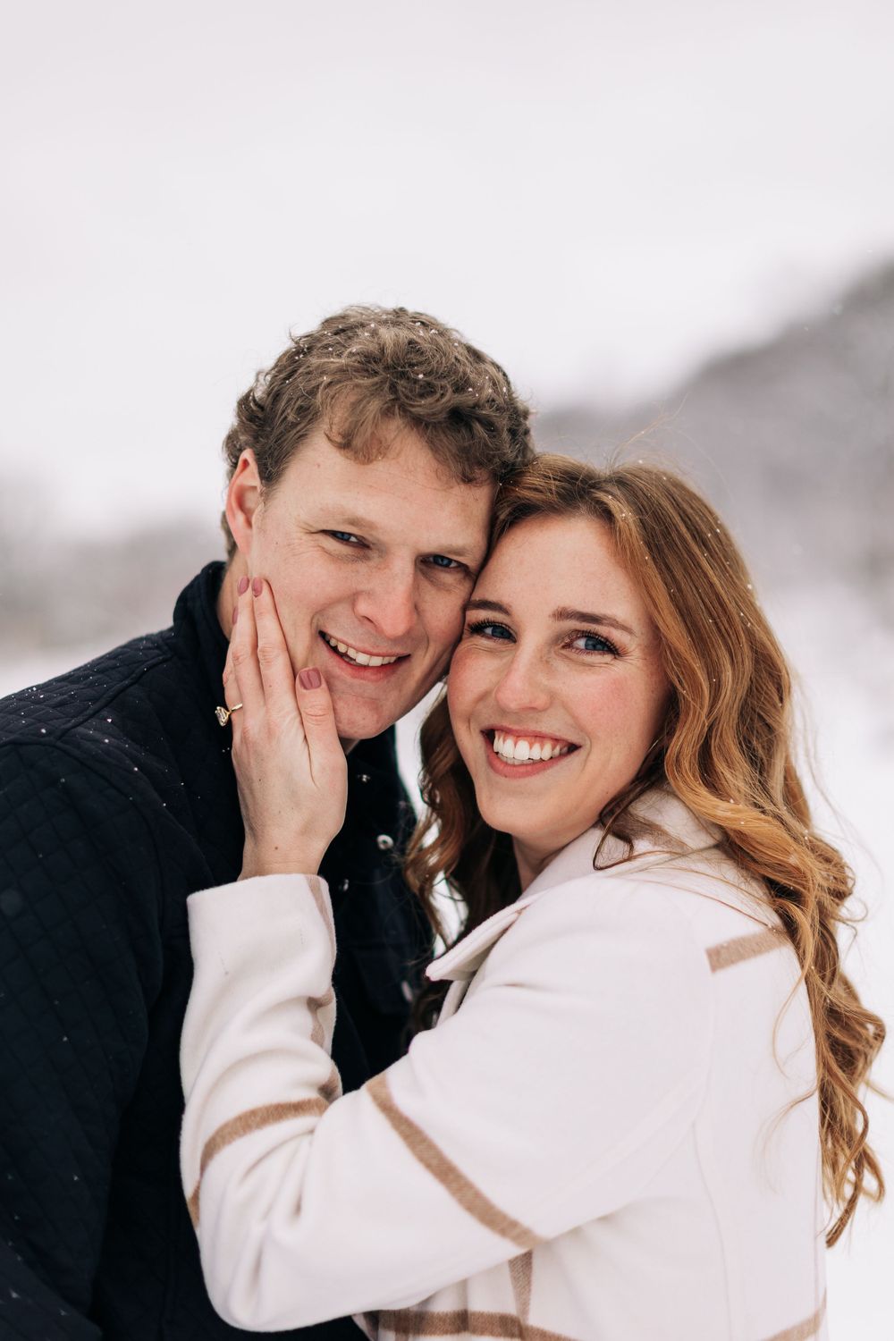 A couple shares a joyful moment together in the snow while wearing winter attire.