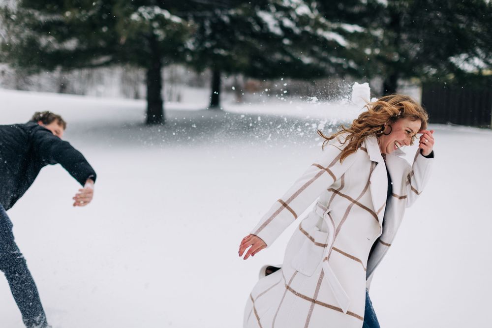 A couple having fun throwing snow at each other in a wintry forest setting.