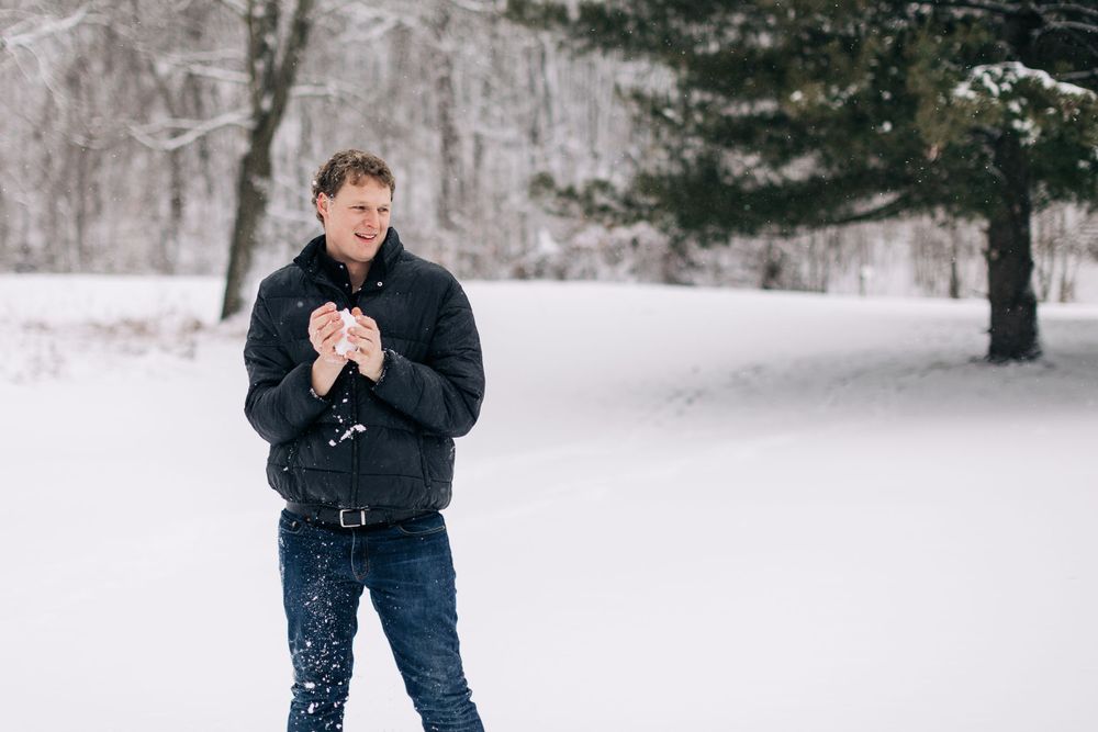 A person holds a device while standing in a snowy winter landscape.