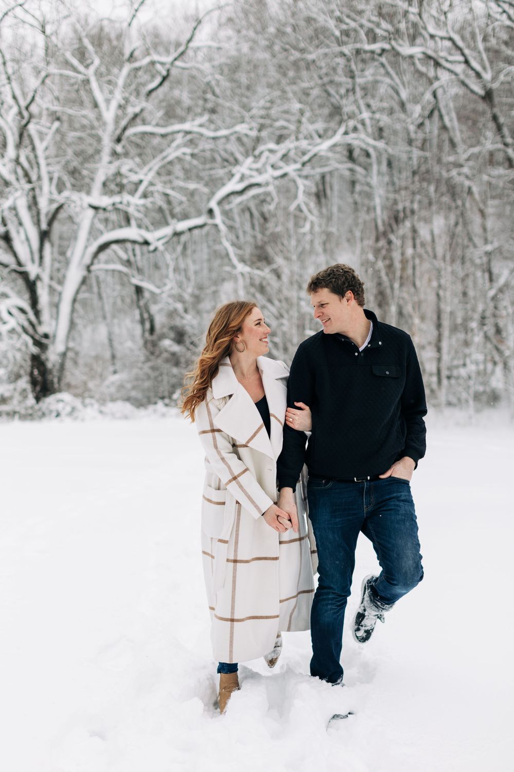 Couple walking together through snow-covered forest path.