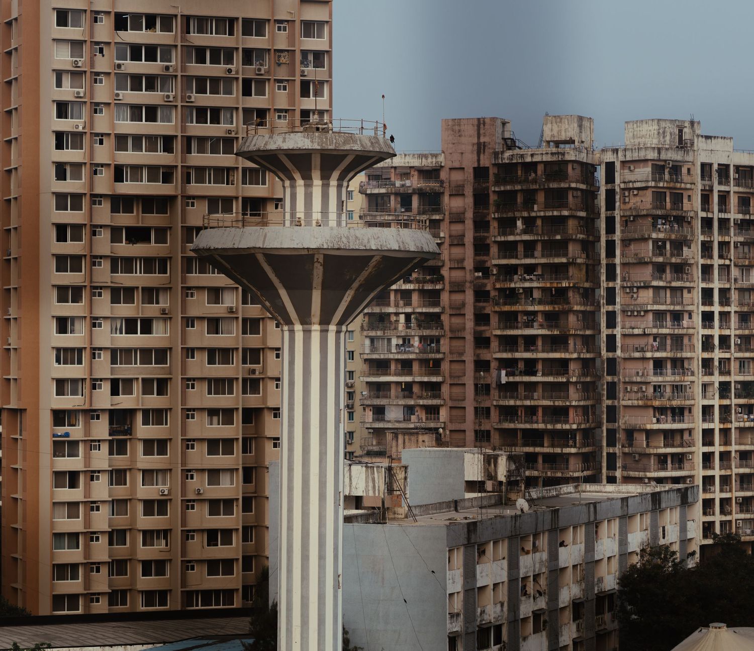Tall concrete water tower standing among residential high-rise apartment buildings in an urban setting.