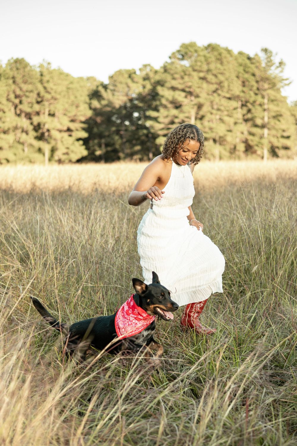 A figure in a white dress and pink boots sits gracefully in a field of tall grass during golden hour.