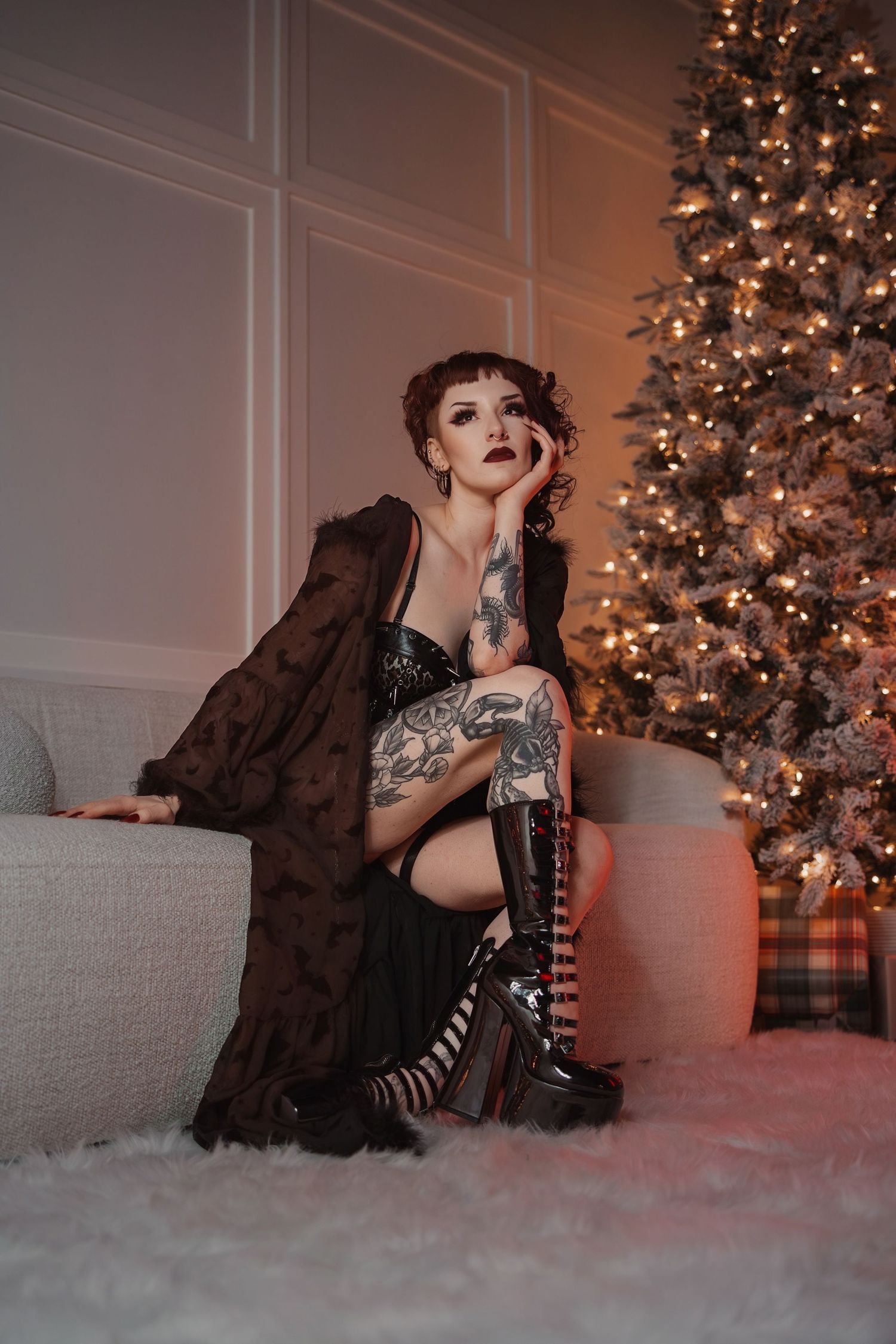 Holiday boudoir photoshoot with illuminated Christmas tree and soft warm lighting in background.
