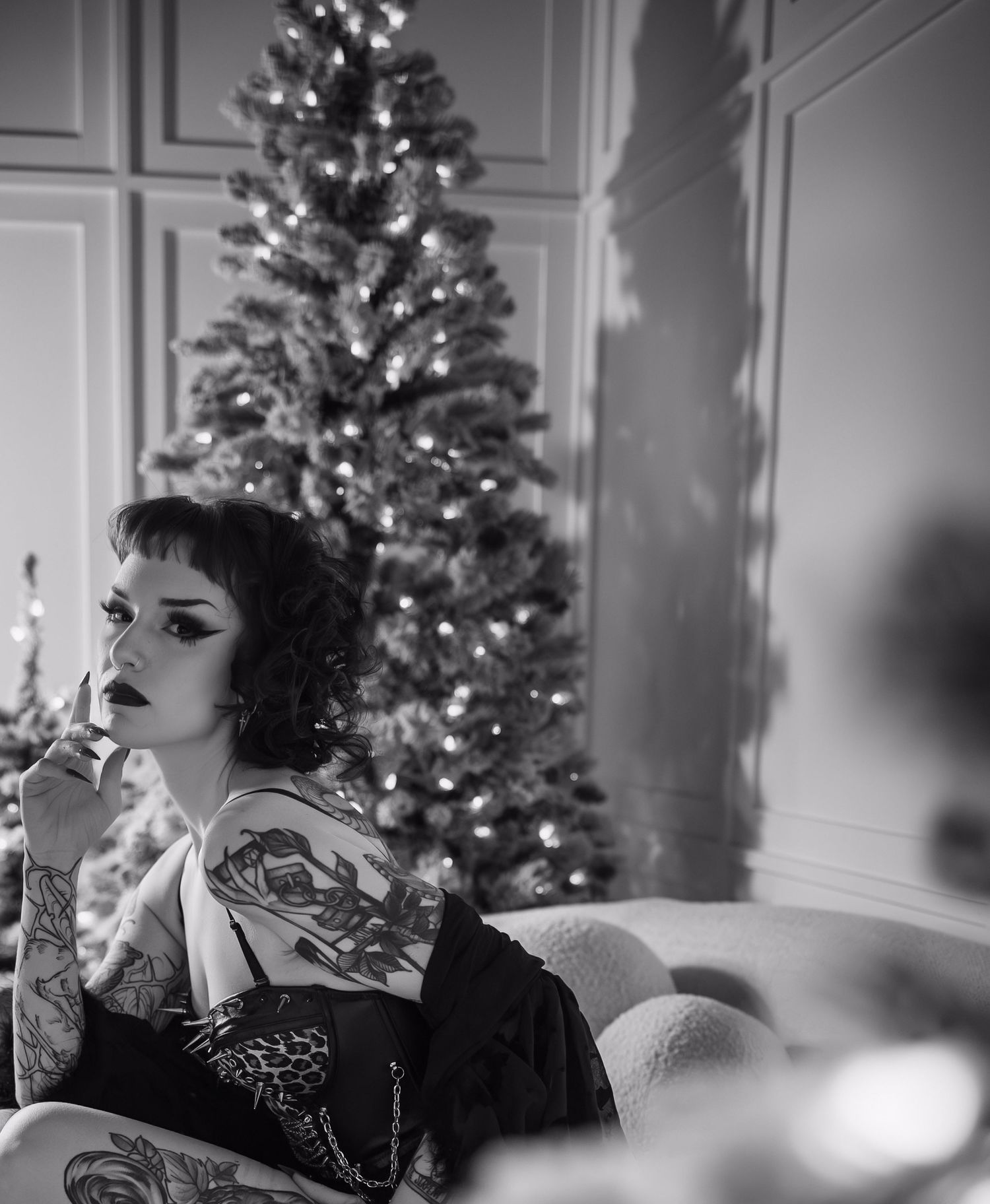 A black and white artistic photograph of a person wearing elegant makeup and a sparkly outfit near Christmas trees.