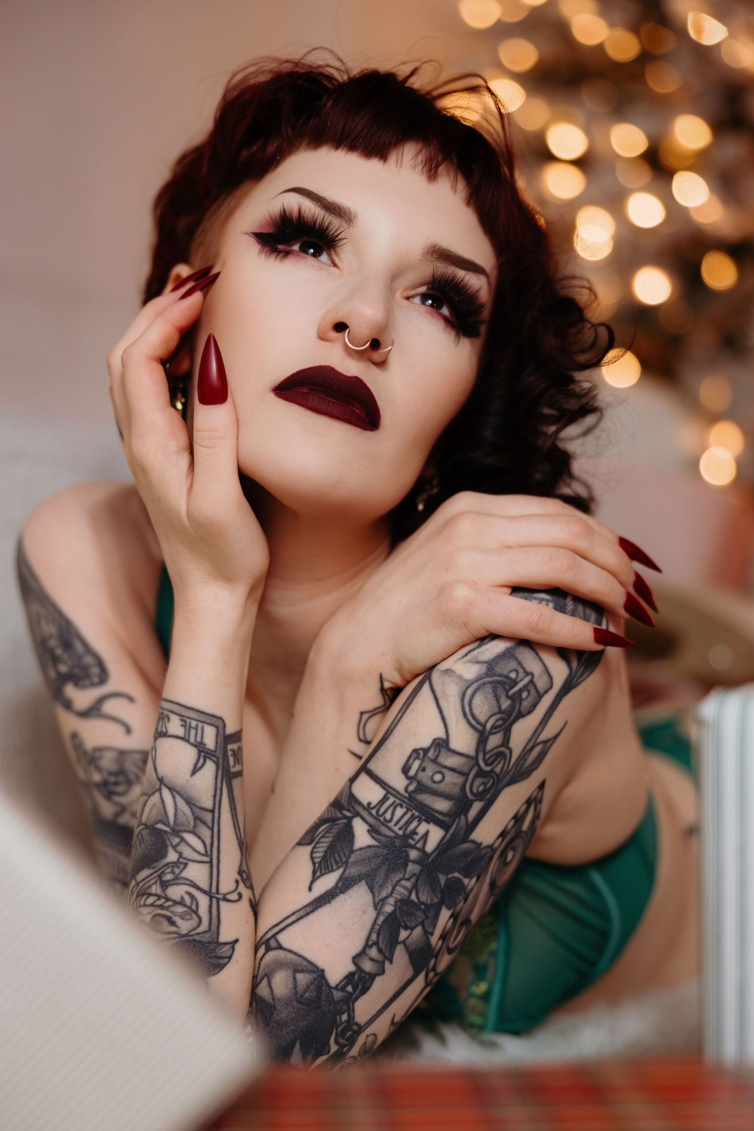 Portrait of tattooed model with dark lipstick and short hair posing against bokeh lights in studio setting.