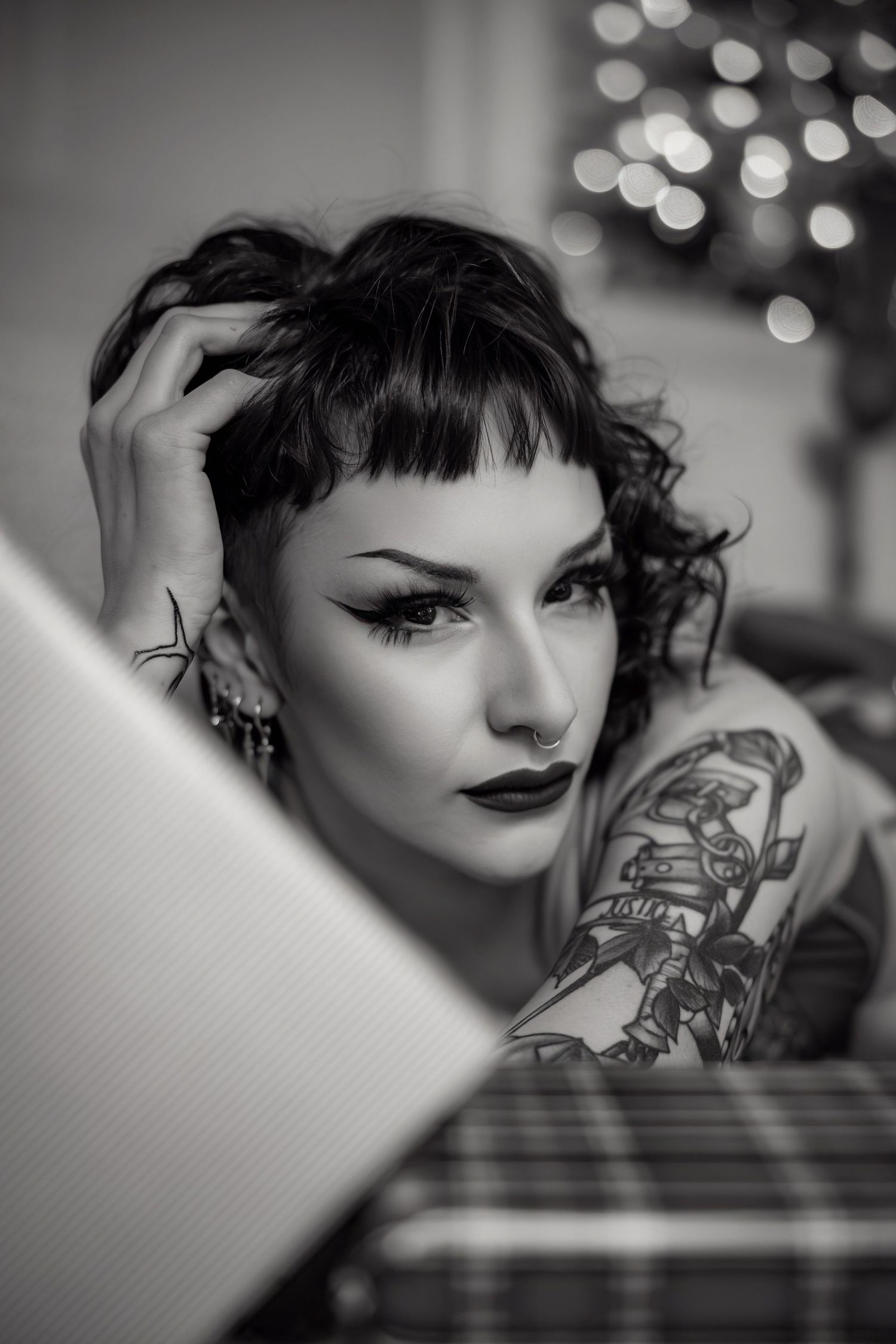 Dramatic black and white portrait showing tattoos and vintage styling with bokeh lights in background.